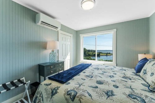 Cozy bedroom with a blue theme, featuring a bed, lamp, and a window view of a scenic landscape.