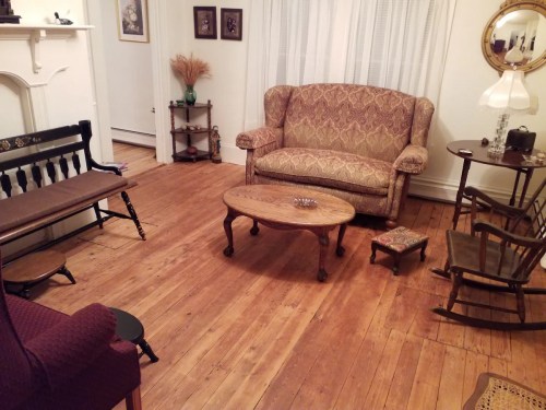 Cozy living room with wooden floors, a patterned couch, a coffee table, and various seating options.