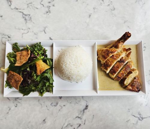 A plate with grilled chicken, white rice, and a side salad with crispy toppings on a marble surface.