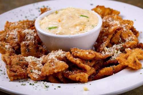 A plate of crispy fried pasta with a bowl of creamy sauce in the center, garnished with herbs and cheese.