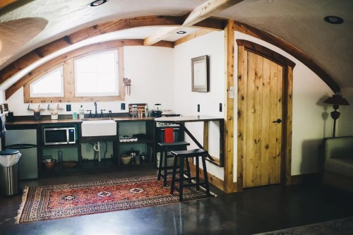 Cozy kitchen area with wooden accents, a sink, and a small dining table under a curved ceiling.