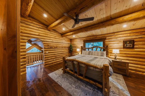 Cozy log cabin bedroom with wooden walls, a large bed, and a ceiling fan, featuring warm lighting and rustic decor.