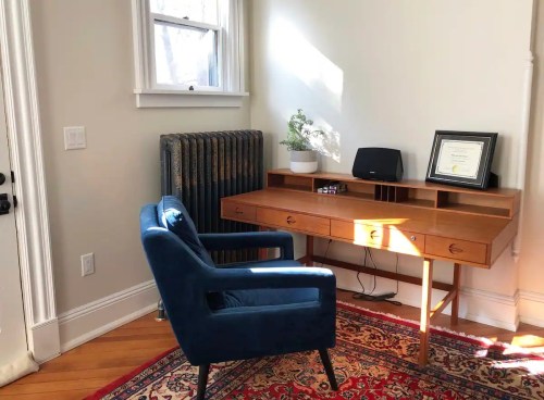 A cozy workspace featuring a blue chair, wooden desk, and a radiator, with natural light streaming in.