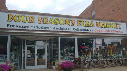 Exterior of Four Seasons Flea Market, featuring a large sign and display of various items for sale.
