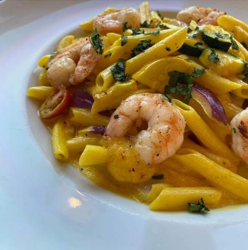 A close-up of pasta with shrimp, cherry tomatoes, and herbs in a creamy sauce, served on a white plate.