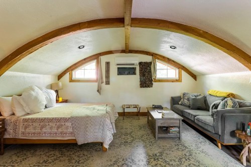 Cozy attic bedroom with a bed, sofa, and wooden beams, featuring natural light and a warm, inviting atmosphere.