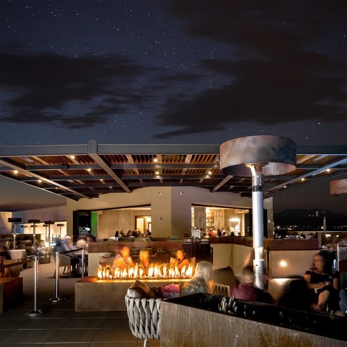 A rooftop lounge at night with a fire pit, seating areas, and a starry sky in the background.