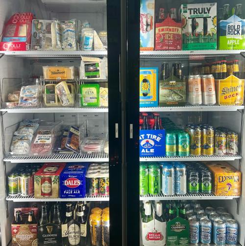 A refrigerator filled with various beverages, including beers, hard seltzers, and snacks, organized on shelves.