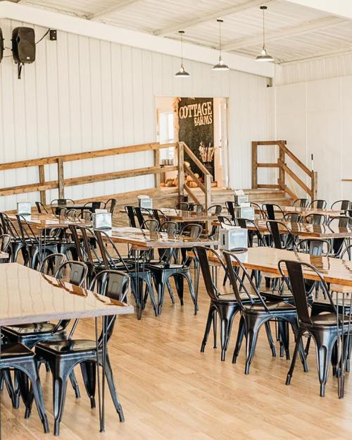 Interior of a spacious dining area with wooden tables and black chairs, featuring a rustic decor and open layout.