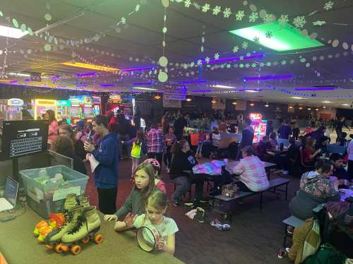 A busy roller skating rink filled with people, games, and festive decorations, with children playing and adults socializing.