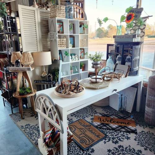 A cozy shop display featuring a white table, decorative items, and a "Welcome" mat, surrounded by various home decor.