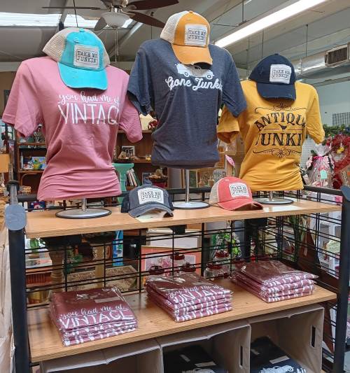Display of colorful t-shirts and hats on mannequins, with a variety of vintage-themed designs in a shop setting.