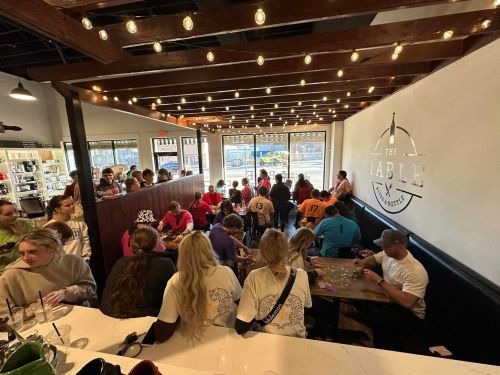 A busy café with people seated at tables, enjoying food and drinks, under warm string lights.