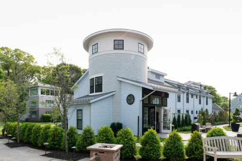 A modern, light-colored building with a circular tower, surrounded by greenery and landscaped pathways.