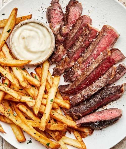 A plate of sliced steak with crispy fries and a small bowl of dipping sauce.