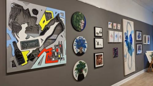 A gallery wall featuring colorful abstract art, portraits, and circular pieces in various styles and mediums.