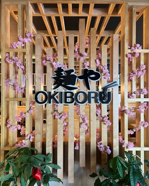 A wooden wall with pink flowers and the sign "OKIBORU" in bold black letters.