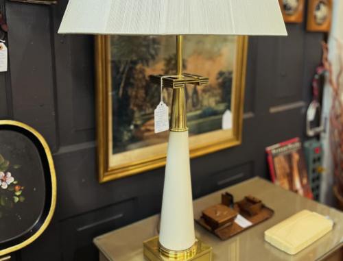 A stylish table lamp with a white base and gold accents, set against a vintage backdrop and decorative items.