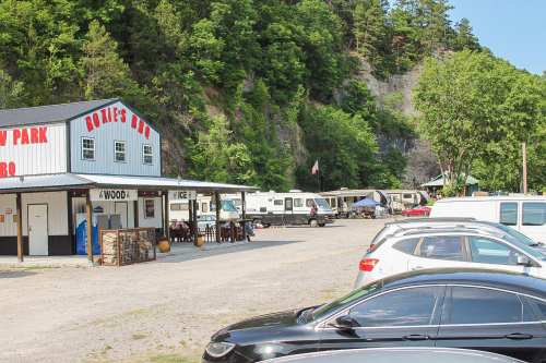 A BBQ restaurant with RVs parked nearby, surrounded by trees and a rocky hillside. Cars are parked in the foreground.