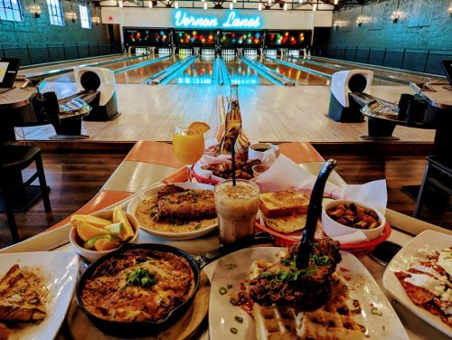 A vibrant bowling alley with a variety of delicious dishes and drinks in the foreground, showcasing a fun dining experience.