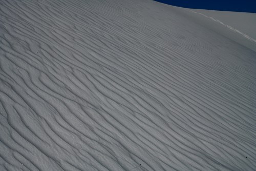 Wavy patterns of fine sand on a dune under a clear blue sky.