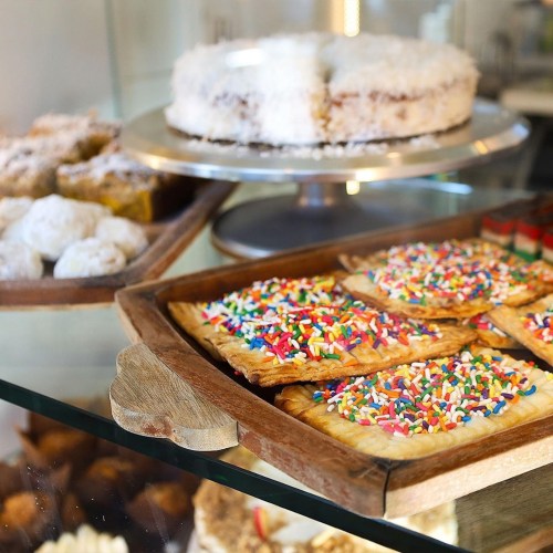 A display of colorful pastries, including sprinkles-covered cookies and a layered cake, in a bakery setting.