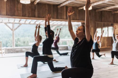 A group of people practicing yoga indoors, with arms raised and focused expressions, in a rustic wooden space.