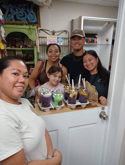 A group of five people smiles together, holding colorful ice cream cups in a cozy shop setting.