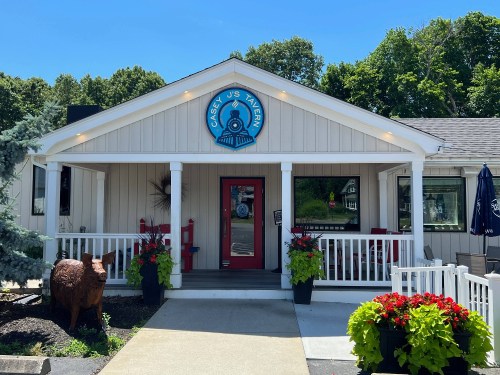 Exterior of Casey J's Tavern featuring a welcoming entrance, colorful flowers, and a blue sign against a sunny backdrop.