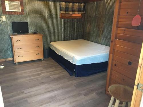 A simple bedroom with a metal wall, wooden furniture, a bed without bedding, and a small TV.