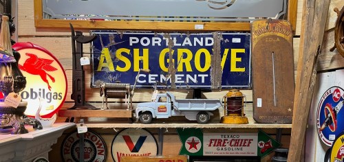 A vintage display featuring a Portland Ash Grove Cement sign, old tools, and various retro gas station signs.