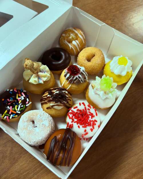 A box of assorted colorful donuts, featuring various toppings like sprinkles, frosting, and decorative designs.