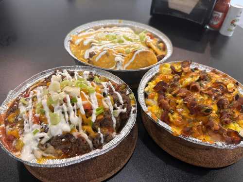 Three bowls of colorful, hearty dishes featuring toppings like sour cream, green onions, and cheese on a black table.