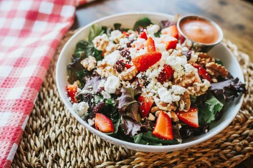 A fresh salad with mixed greens, strawberries, walnuts, feta cheese, and a side of dressing, on a woven placemat.