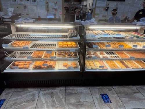 A display case filled with various baked goods, including cookies, pastries, and donuts, in a bakery setting.