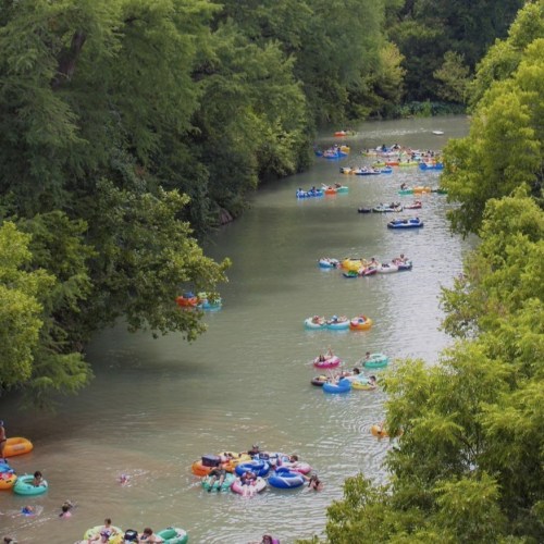 A river filled with people floating on colorful inner tubes surrounded by lush green trees.