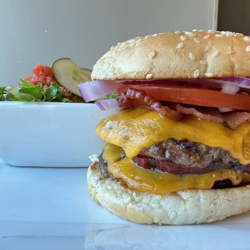 A juicy cheeseburger with melted cheddar, bacon, lettuce, tomato, and onion, served with a side of fresh salad.
