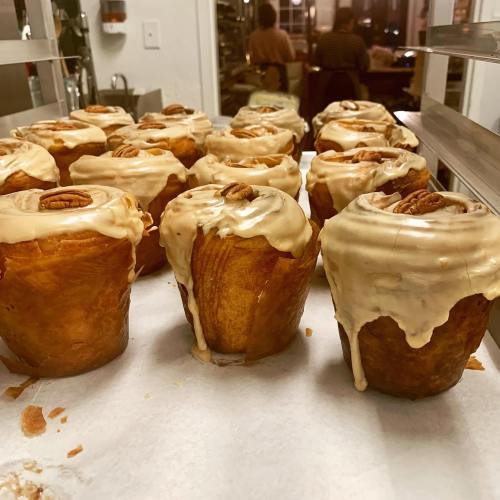 Freshly baked cinnamon rolls with creamy frosting and pecans, arranged on a baking tray.