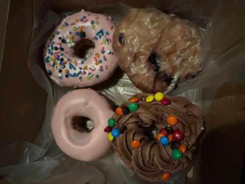 A box of four donuts: one pink with sprinkles, one glazed, one plain, and one chocolate with colorful candy.