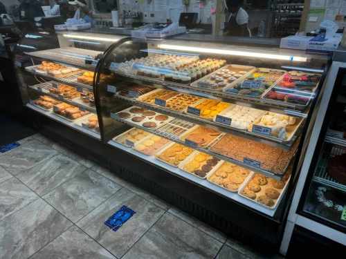A display case filled with various baked goods, including cookies, pastries, and cupcakes, in a bakery setting.