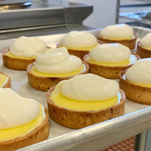 A tray of freshly baked tartlets with a creamy topping and a yellow custard filling.