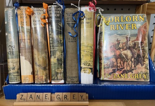 A collection of Zane Grey books displayed on a shelf, with colorful ribbons and a wooden block spelling "ZANE GREY."