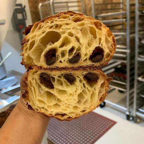 A hand holding a freshly cut croissant, revealing its flaky layers and chocolate filling inside.