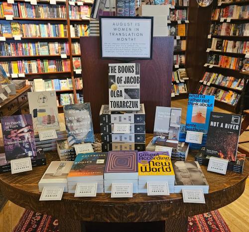 Display of books celebrating Women in Translation Month, featuring various titles and authors on a wooden table in a bookstore.