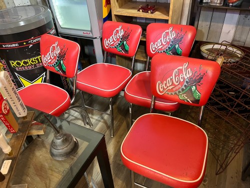 Four vintage red Coca-Cola chairs with playful graphics, arranged in a rustic setting.