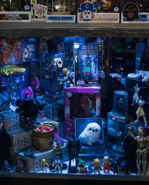 A display case filled with various action figures, collectibles, and toys, illuminated by blue light.