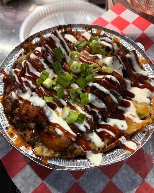 A foil dish filled with loaded nachos topped with barbecue sauce, sour cream, green onions, and crispy toppings.