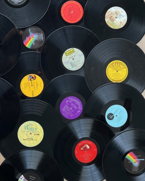 A collection of vinyl records scattered on a surface, featuring various labels and colorful center stickers.