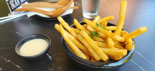 A bowl of golden fries garnished with herbs, accompanied by a small dish of dipping sauce and chopsticks.