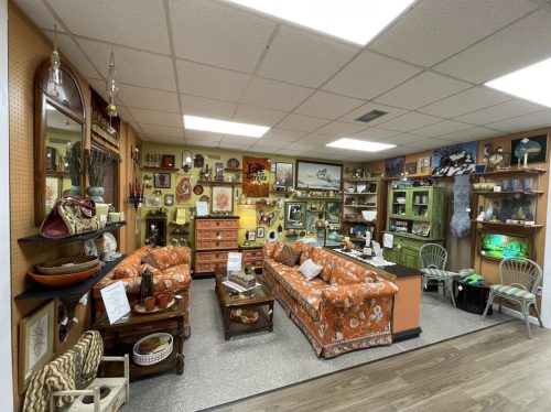 A cozy vintage shop interior featuring orange floral sofas, shelves of decor, and various art pieces on the walls.